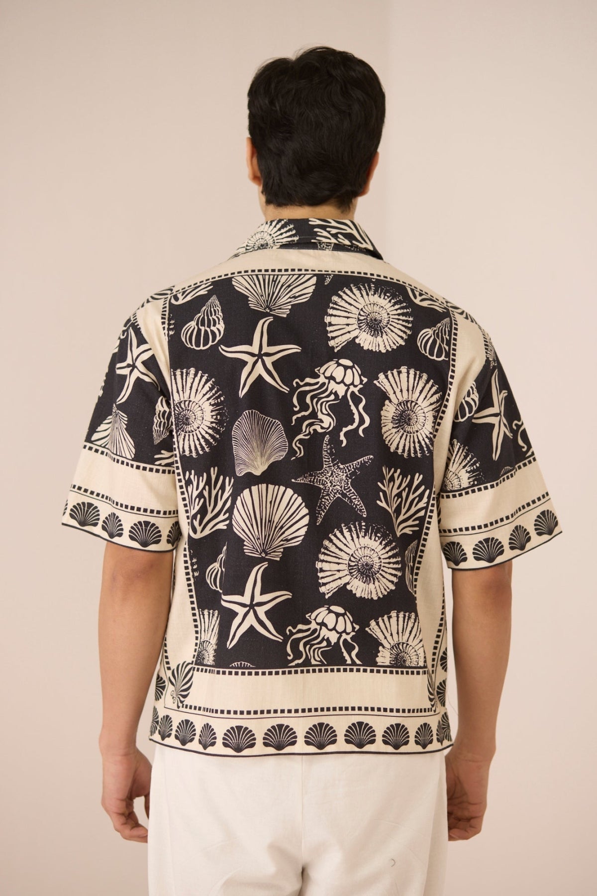 Person wearing a black and white patterned shirt with seashell design on a beige background Calling June