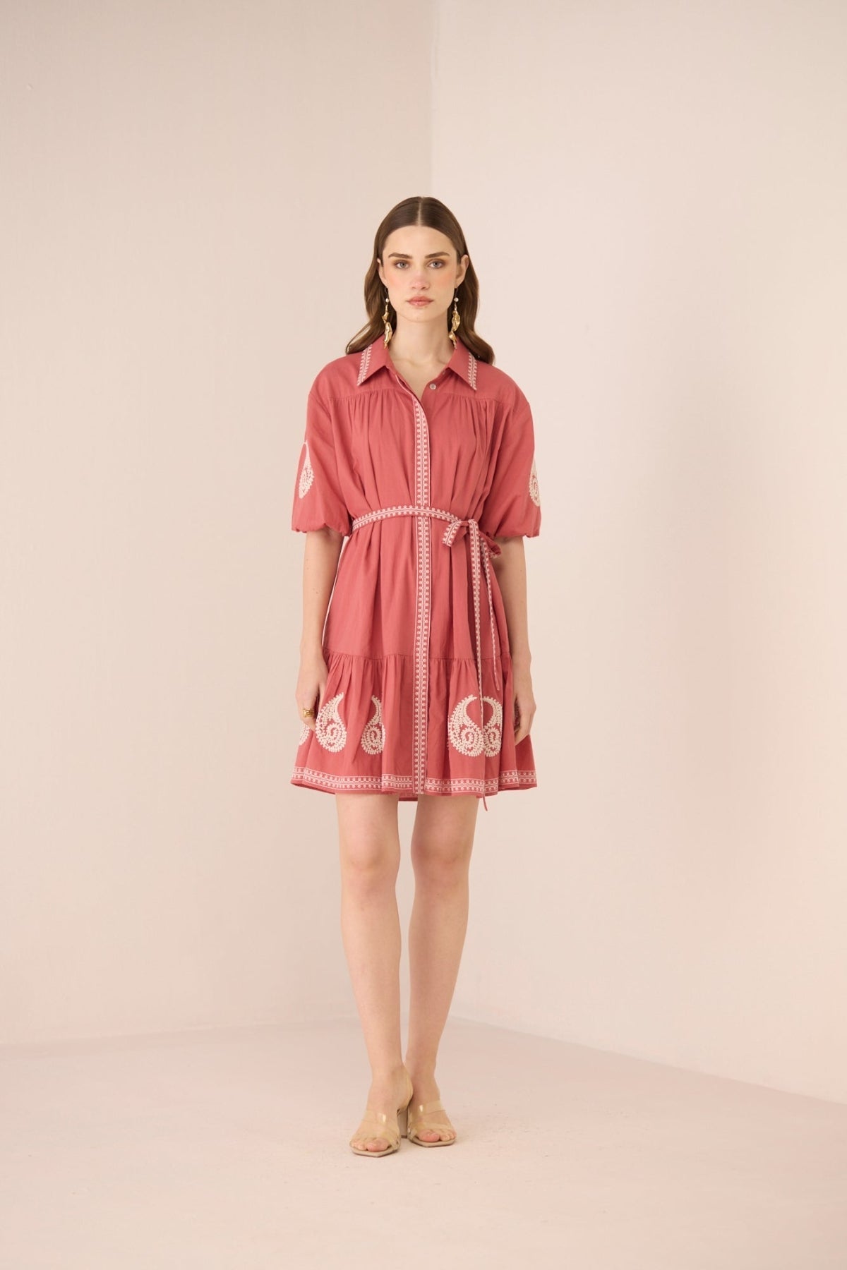 Woman wearing a pink dress with white embroidery on a beige background Calling June