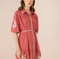 Woman wearing a pink dress with white embroidery on a beige background Calling June