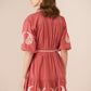 Woman wearing a red dress with white embroidery on a beige background Calling June