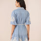 Woman wearing a blue dress with white embroidery on a beige background Calling June