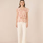 Woman wearing a floral blouse and white pants on a beige background Calling June