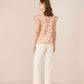 Woman wearing a floral top and white pants on a beige background Calling June