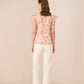 Woman wearing a floral top and white pants on a beige background Calling June