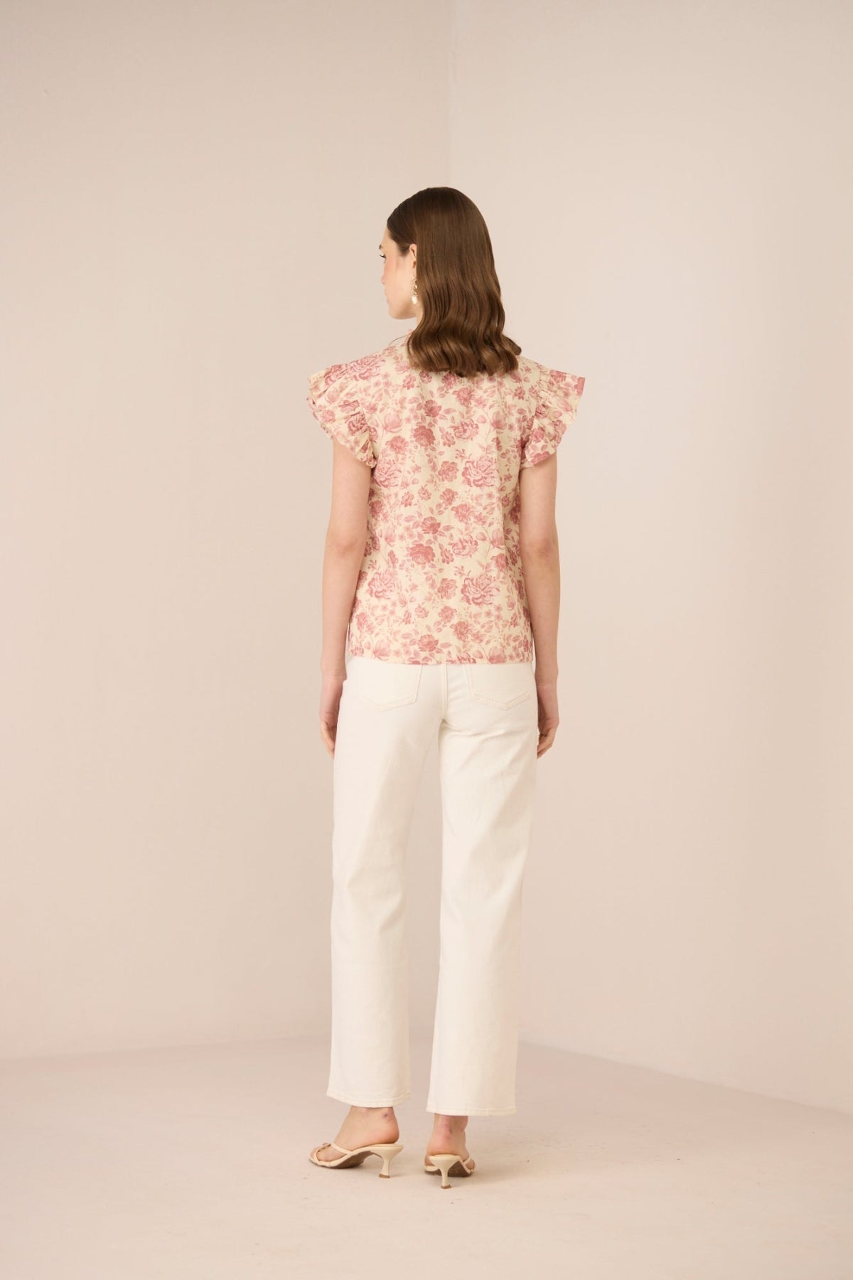 Woman wearing a floral top and white pants on a beige background Calling June