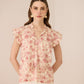 Woman wearing a floral blouse with ruffled sleeves against a beige background Calling June