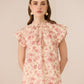 Woman wearing a floral blouse with ruffled sleeves against a beige background Calling June