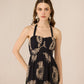Woman wearing a black dress with gold floral patterns on a beige background Calling June