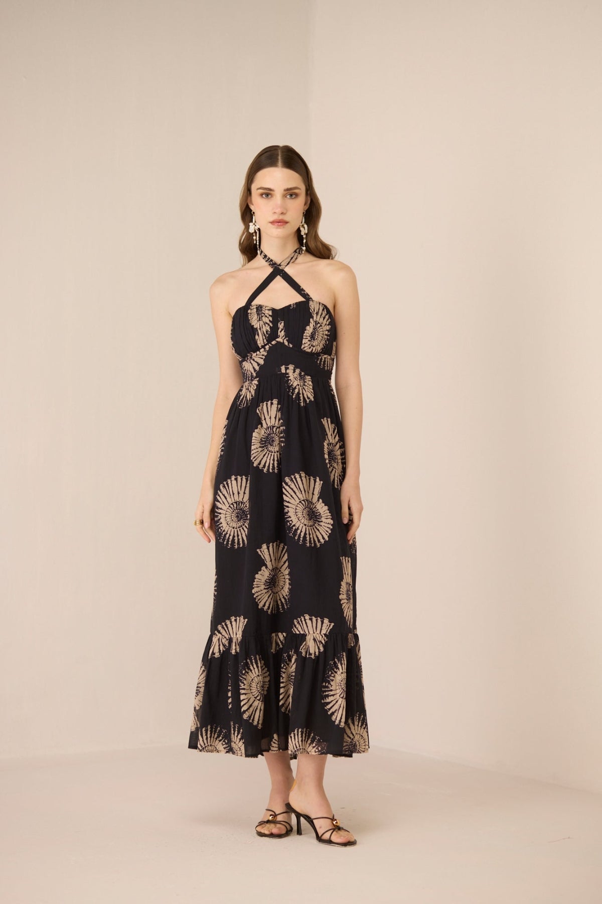 Woman wearing a black dress with gold floral patterns on a beige background Calling June