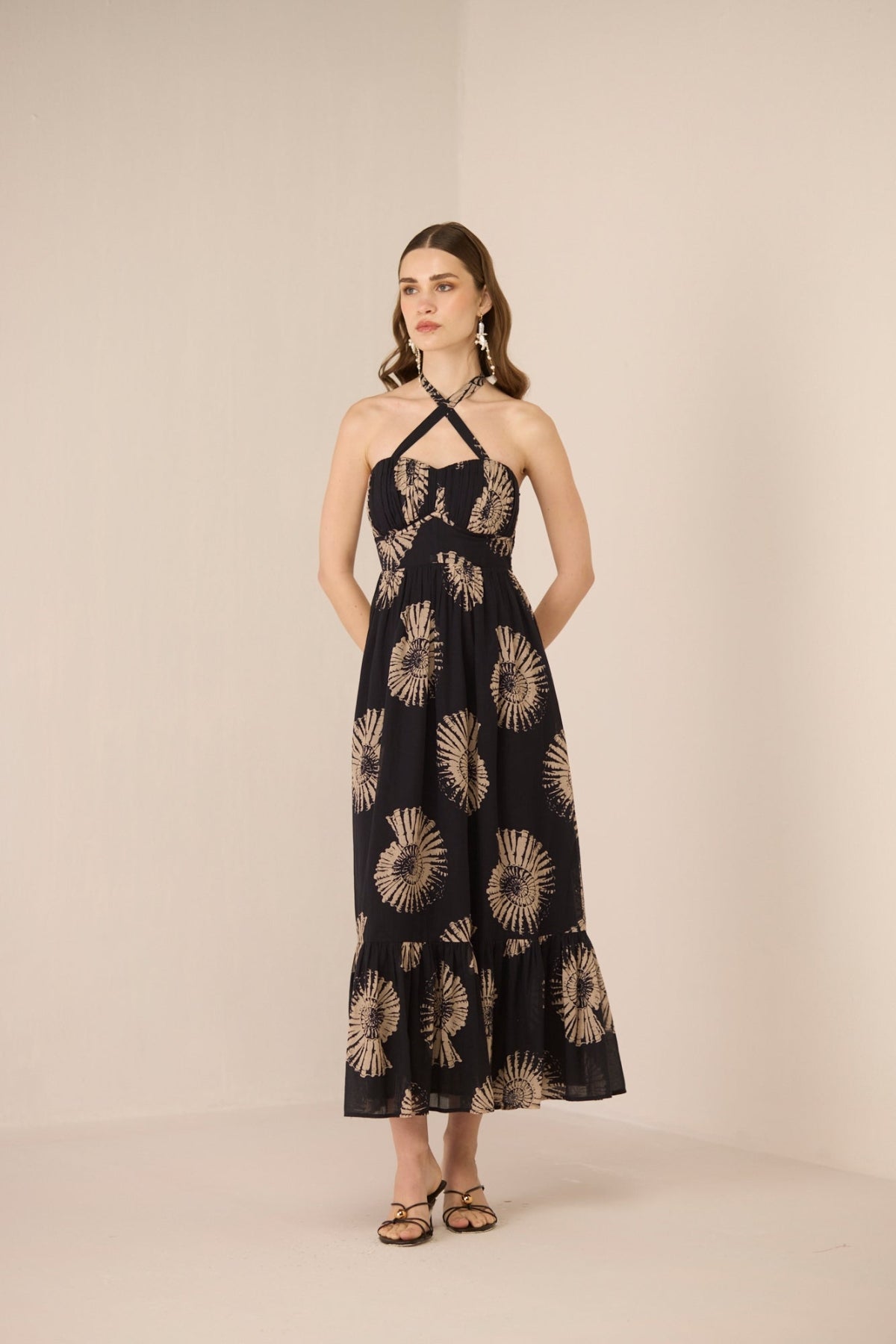 Woman wearing a black dress with gold floral patterns on a beige background Calling June