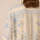 Beige shirt with blue floral patterns worn by a person against a beige background Calling June