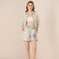 Woman wearing a light blue shirt, white top, and floral shorts on a beige background Calling June