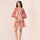 Woman wearing a pink dress with white lace details on a plain background Calling June