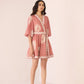 Woman wearing a pink dress with white patterns on a plain background Calling June