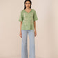 Woman wearing a green embroidered top and light blue jeans on a beige background Calling June