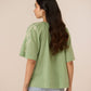 Woman wearing a green top with floral embroidery on a beige background Calling June