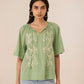 Woman wearing a green embroidered blouse with light blue jeans against a beige background Calling June
