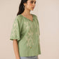 Woman wearing a green embroidered blouse against a beige background Calling June