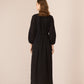 Woman wearing a black dress with long sleeves and a belt, standing against a plain background. Calling June