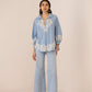 Woman wearing a light blue embroidered outfit on a beige background Calling June