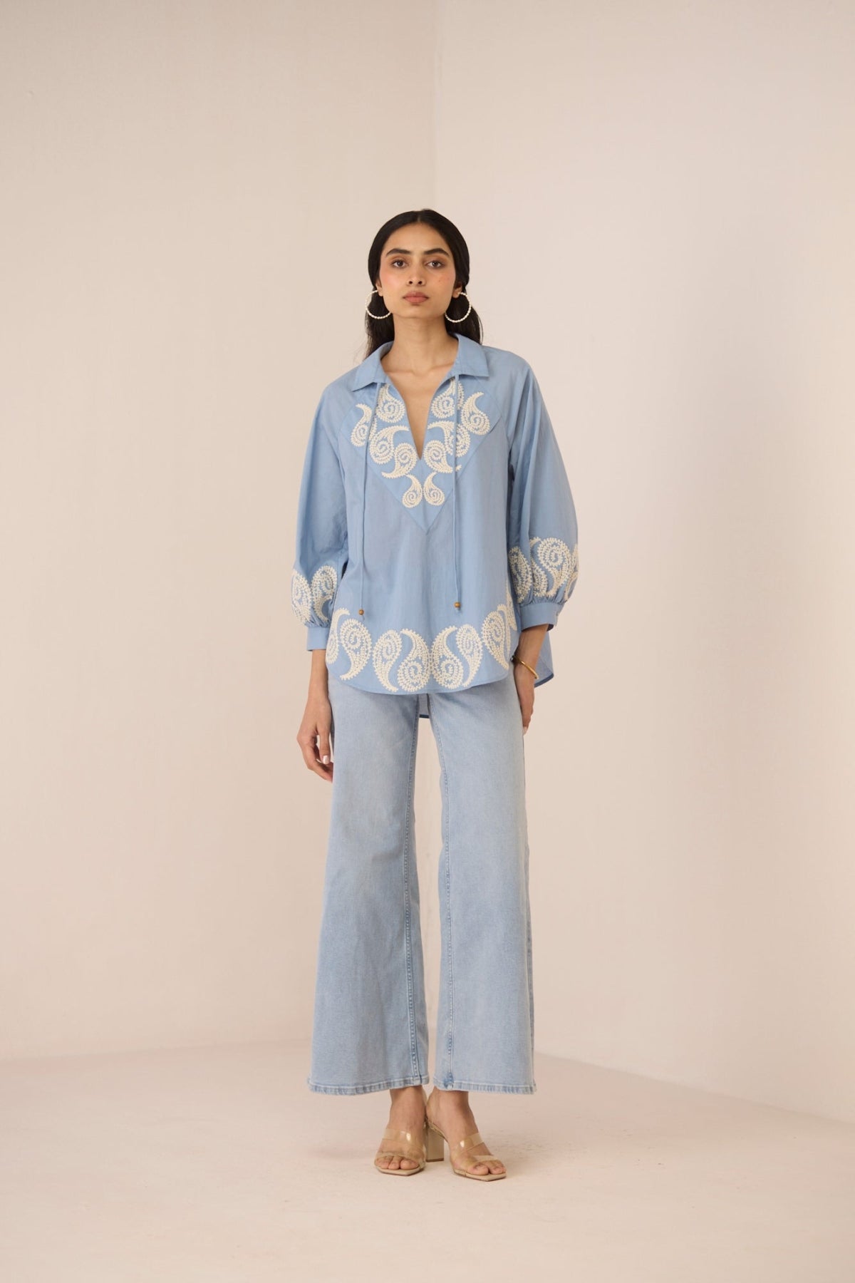 Woman wearing a light blue embroidered outfit on a beige background Calling June
