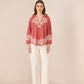 Woman wearing a red embroidered blouse and white pants on a beige background Calling June