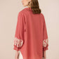Woman wearing a pink blouse with lace details on sleeves against a beige background Calling June