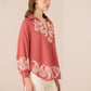 Woman wearing a pink blouse with white embroidery on a beige background Calling June