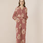 Woman wearing a pink floral jumpsuit on a beige background Calling June