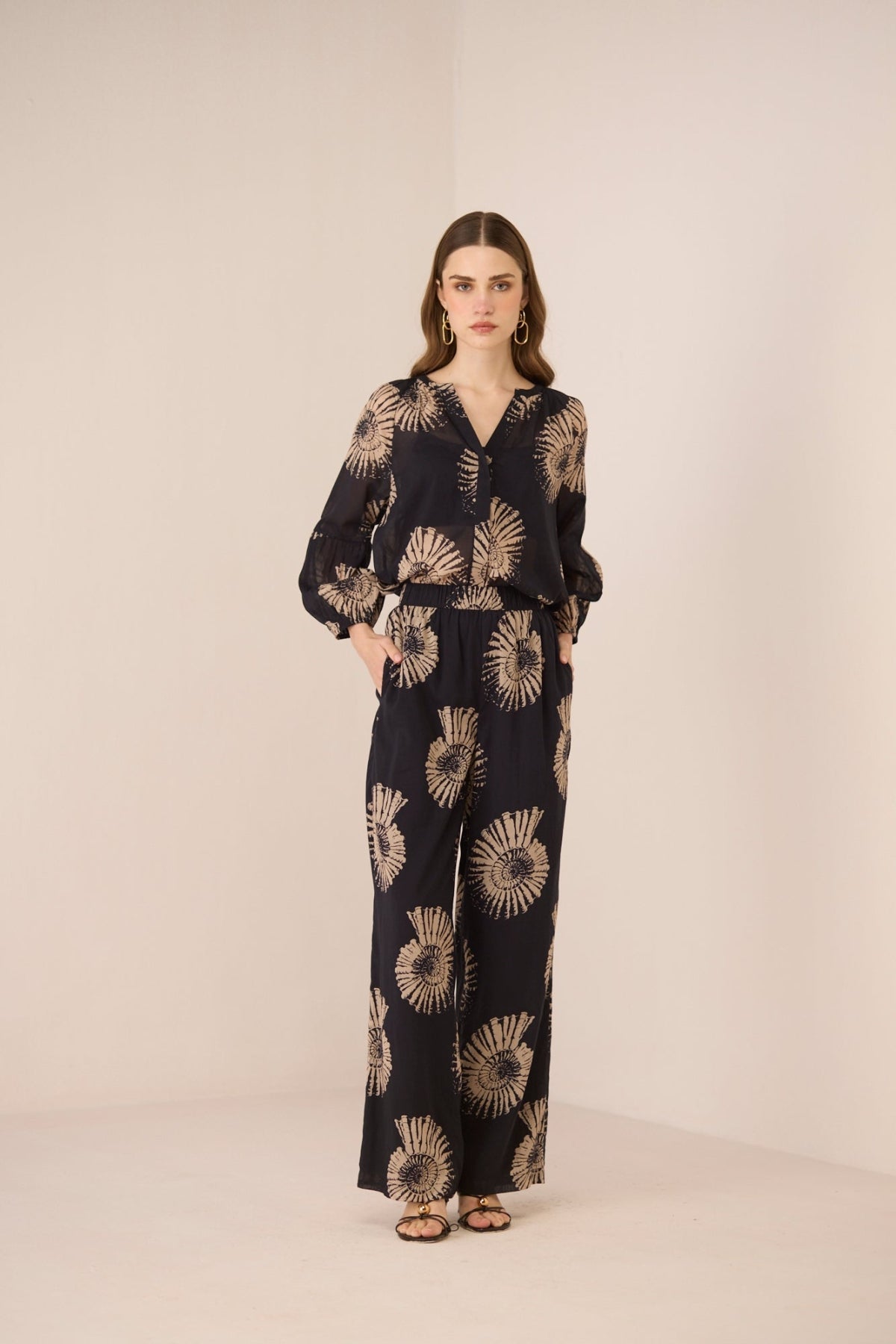 Woman wearing a black jumpsuit with gold sunflower patterns on a beige background Calling June