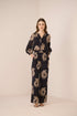 Woman wearing a black jumpsuit with gold sunflower patterns on a beige background Calling June