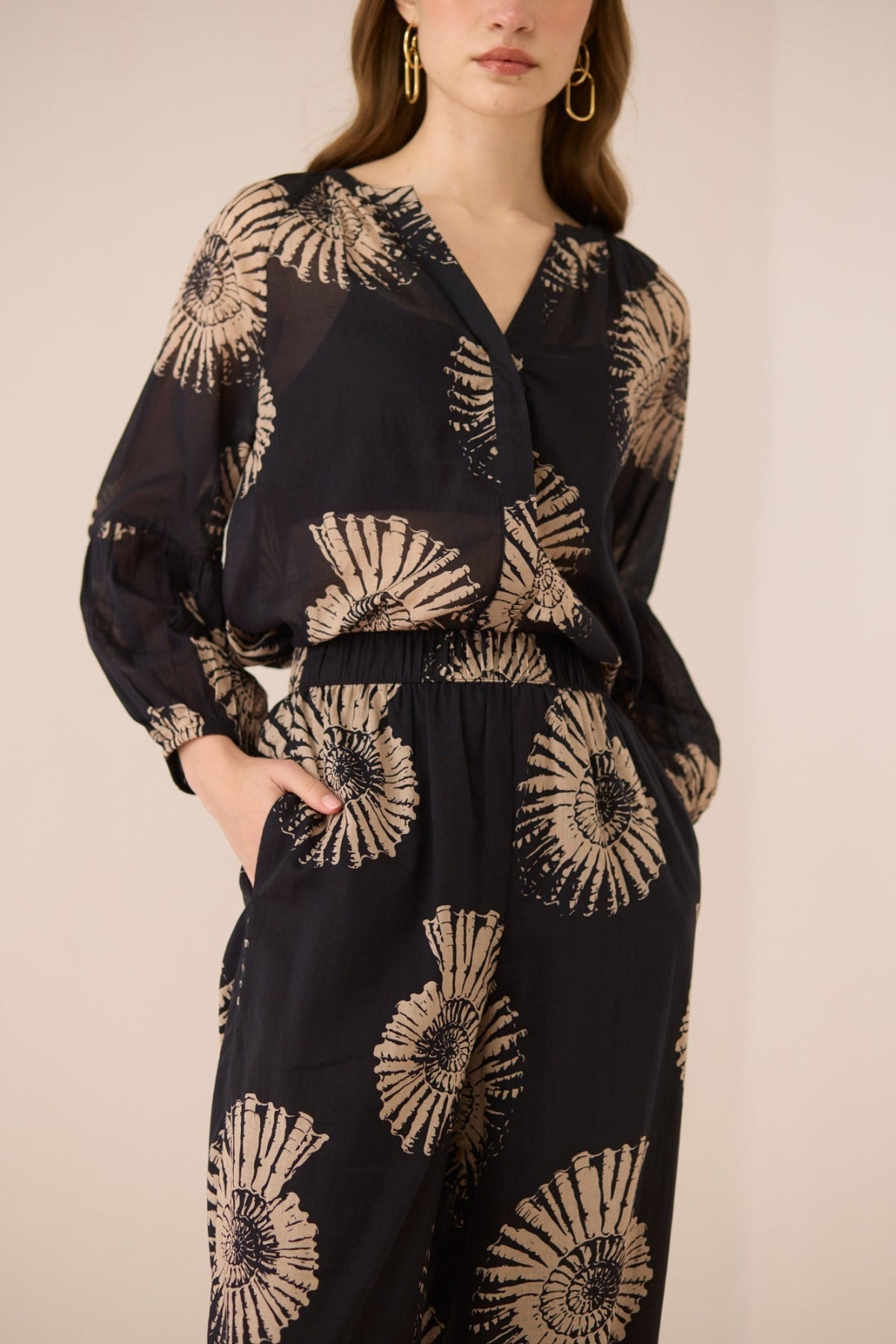Woman wearing a black outfit with gold floral patterns on a beige background Calling June