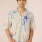 Man wearing a light-colored shirt with starfish and shell patterns on a plain background Calling June