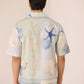 Person wearing a light-colored shirt with blue starfish and shell designs on a plain background Calling June