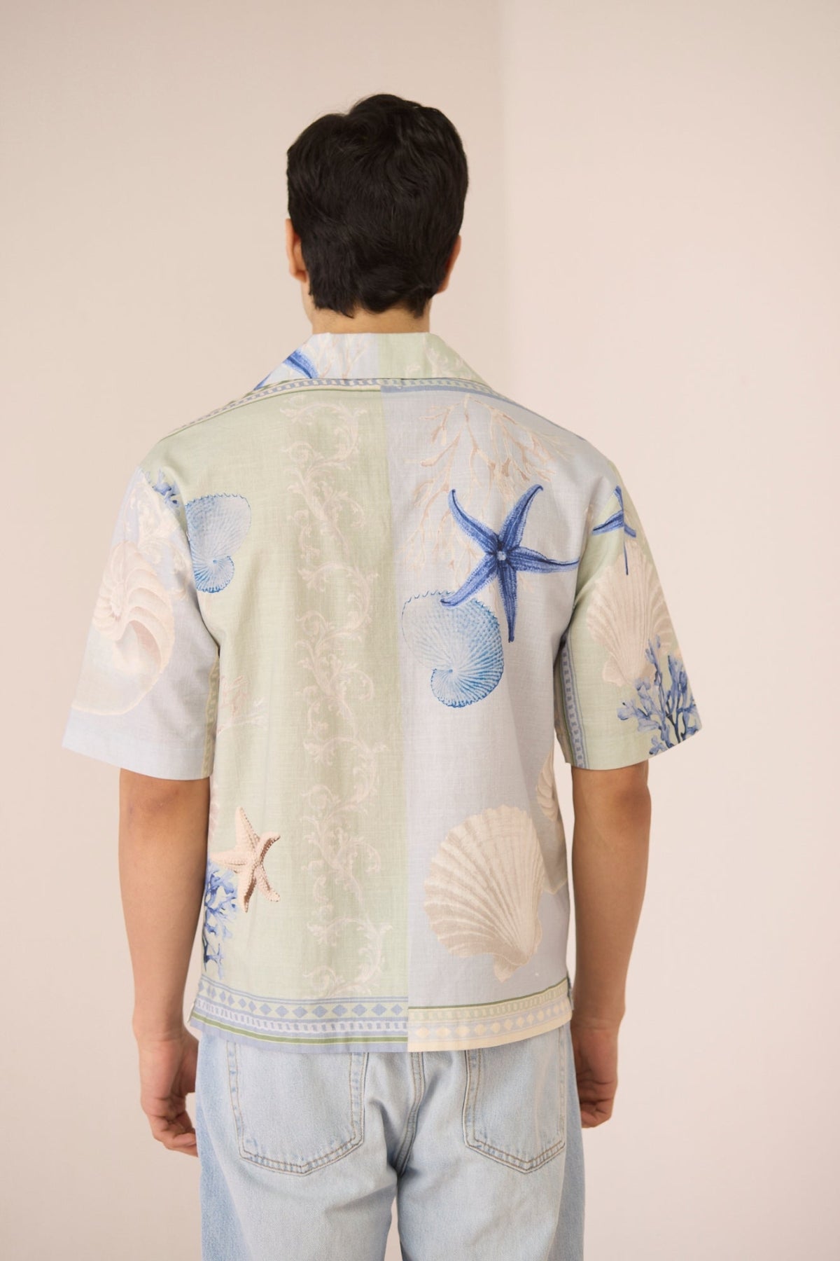 Person wearing a light-colored shirt with blue starfish and shell designs on a plain background Calling June