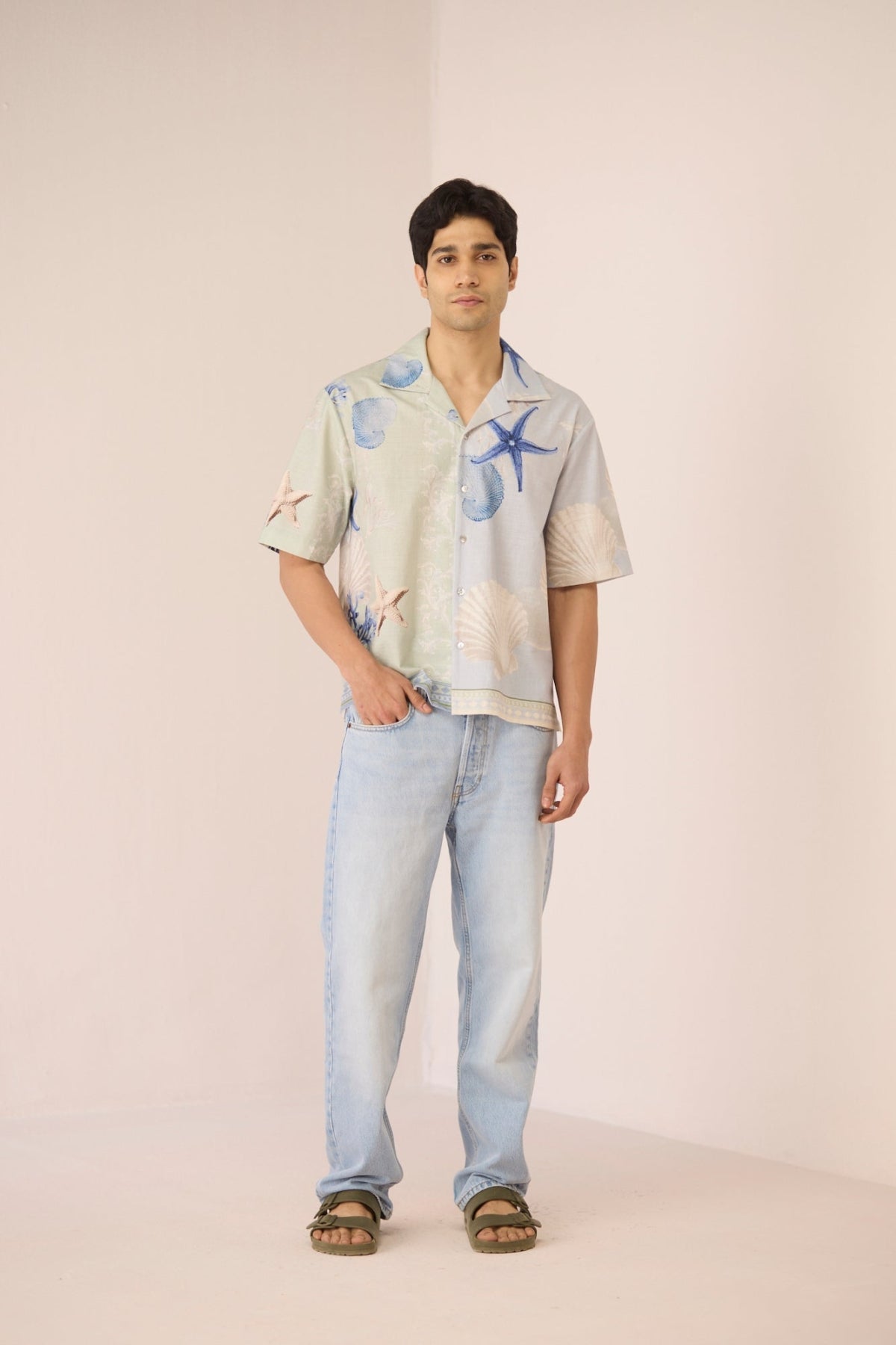 Man wearing a patterned shirt and jeans on a plain background Calling June