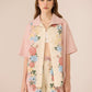 Woman wearing a floral shirt and shorts set with a pink jacket on a beige background Calling June