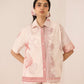 Woman wearing a matching pink and white outfit with floral patterns on a plain background Calling June