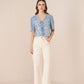 Woman wearing a blue embroidered blouse and white pants on a beige background Calling June