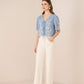 Woman wearing a blue floral blouse and white pants on a beige background Calling June