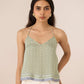 Woman wearing a green patterned top with white pants against a beige background Calling June