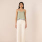 Woman wearing a green patterned top and white pants against a beige background Calling June