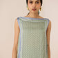Woman wearing a green sleeveless top with a patterned border against a beige background Calling June