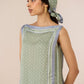 Woman wearing a green and blue patterned outfit with a matching headscarf against a beige background Calling June
