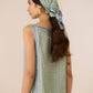 Woman wearing a green and white patterned top with a matching headscarf on a beige background Calling June