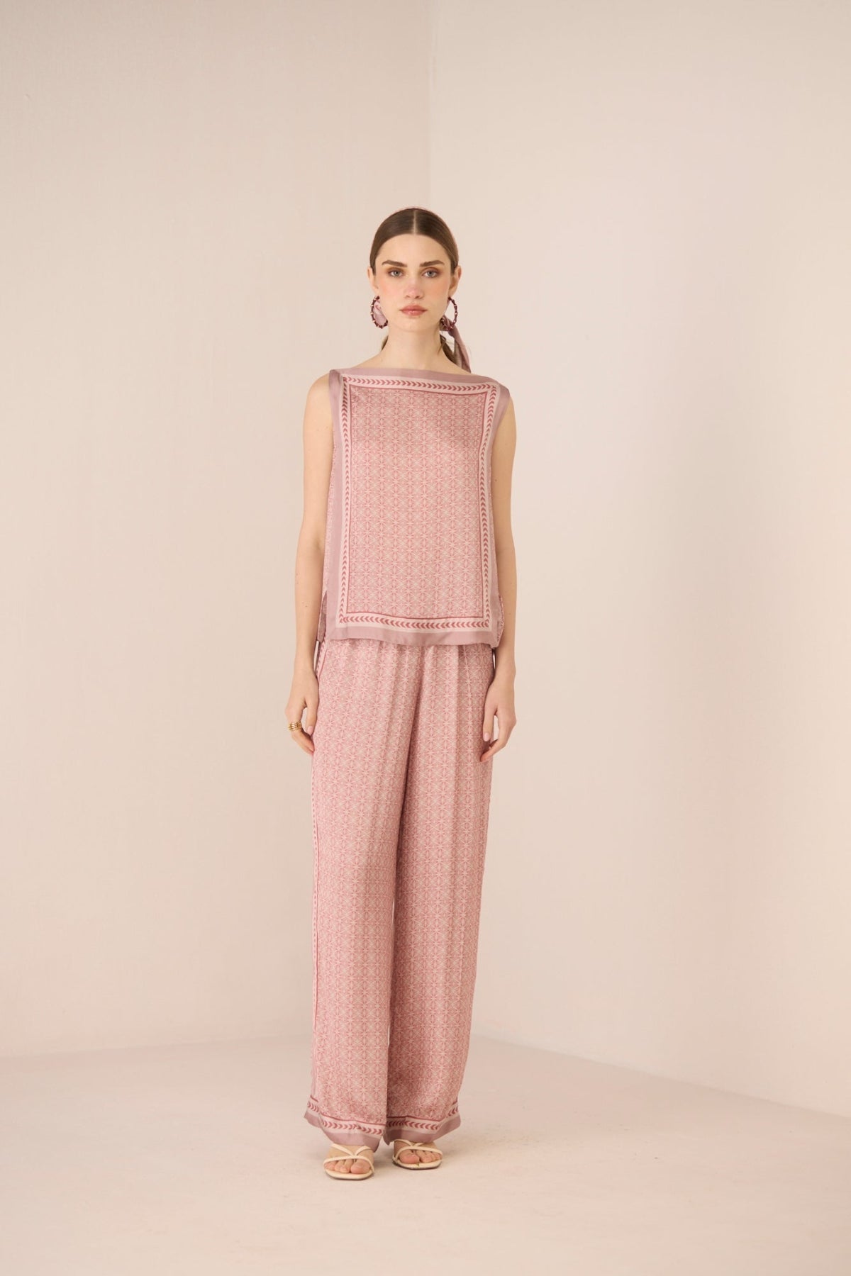 Woman wearing a pink textured sleeveless top and pants on a beige background Calling June