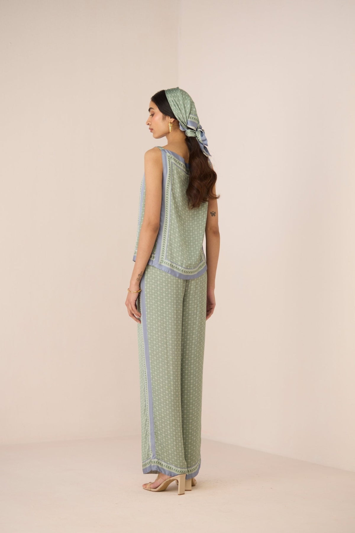 Woman wearing a green patterned outfit with a matching headscarf on a beige background Calling June